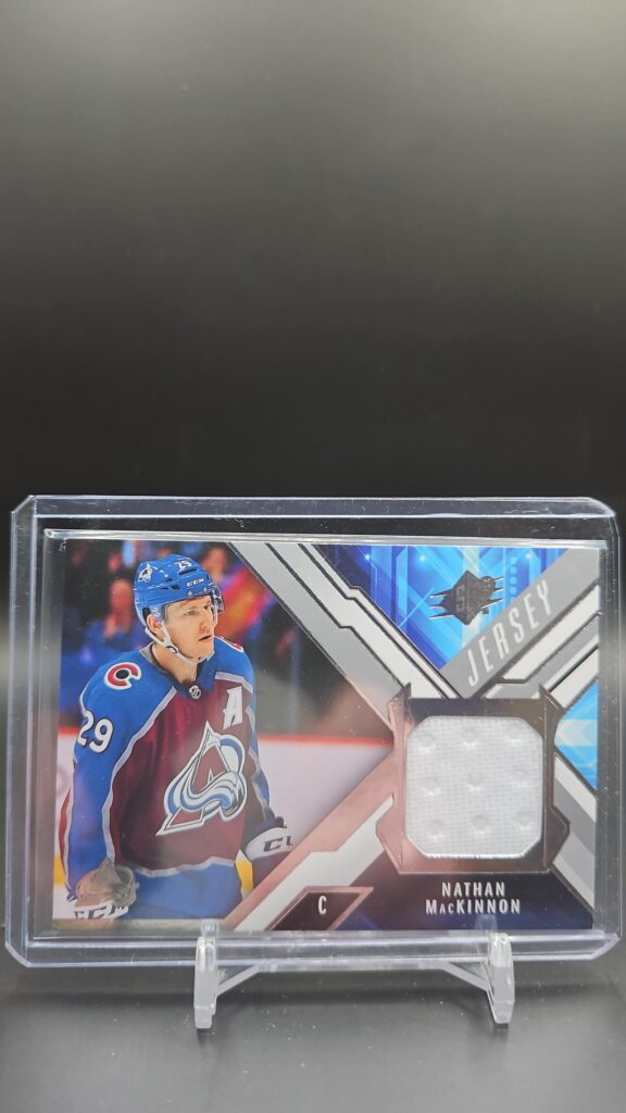 2021-22 Upper Deck SPx Jersey Nathan MacKinnon card #J-NM, Mint condition, Colorado Avalanche, game-used memorabilia, top collectible for NHL fans.