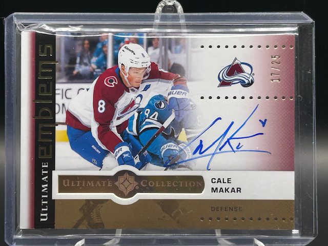 Front of 2025-26 Upper Deck Ultimate Collection Cale Makar Ultimate Emblems Autograph Gold hockey card serial numbered /25